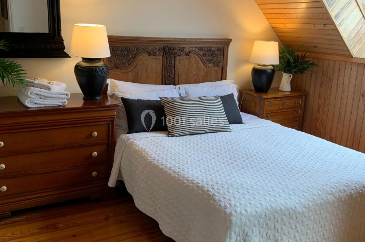 Chambre avec lit double, couvre-lit blanc, coussins décoratifs, meubles en bois et lampe sur chaque table de chevet.