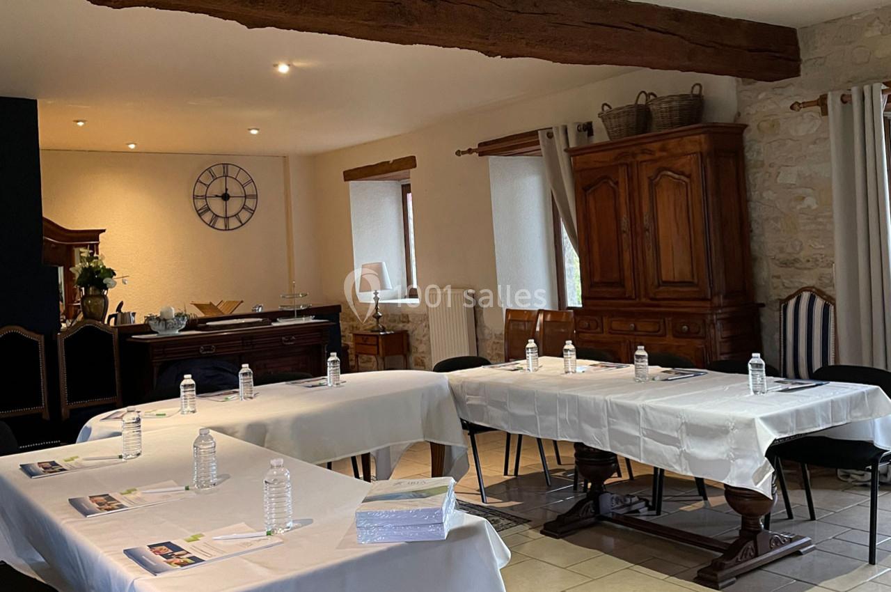 Salle de réunion lumineuse avec tables disposées en U, nappées de blanc, bouteilles d'eau et documents posés.