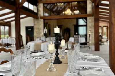 Table élégamment dressée avec chandeliers noirs, verres en cristal et nappes blanches dans une salle au style rustique.