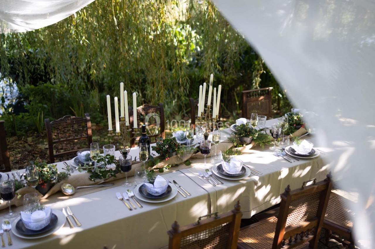 Table de réception élégamment dressée en extérieur, ornée de bougies, vaisselle raffinée et décorations végétales.