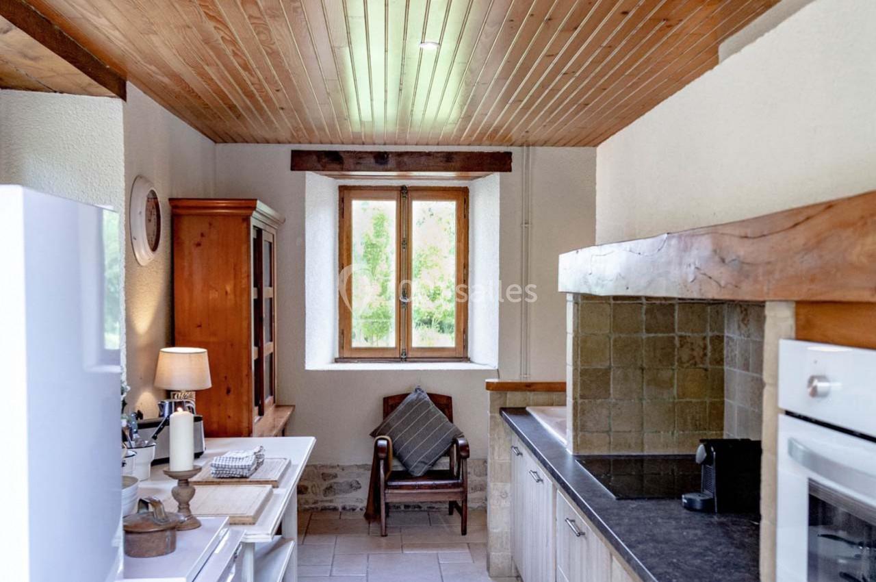Cuisine rustique avec plafond en bois, fenêtre lumineuse, meubles en bois, plan de travail noir et four encastré.
