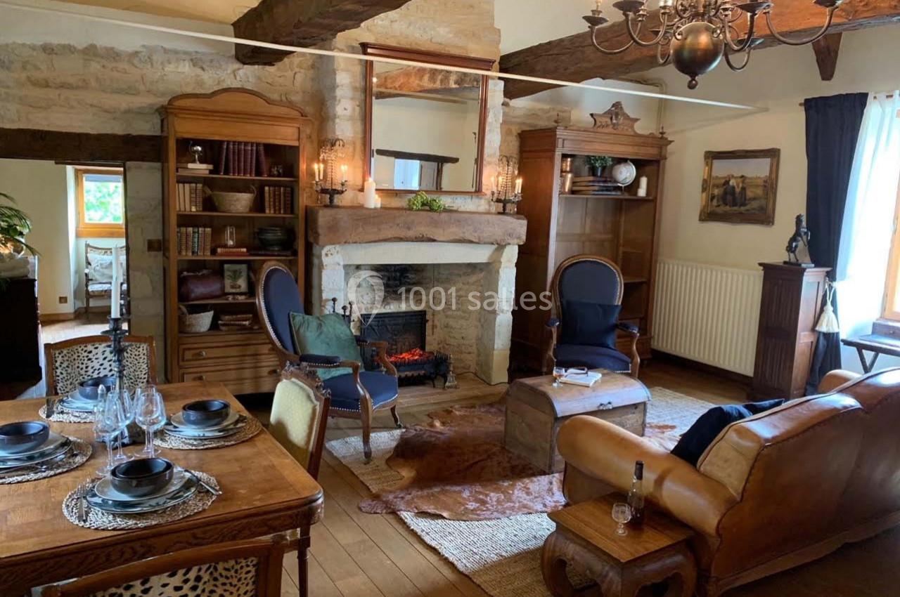 Salon rustique avec poutres apparentes, cheminée en pierre, mobilier en bois et fauteuils autour d'une table basse.