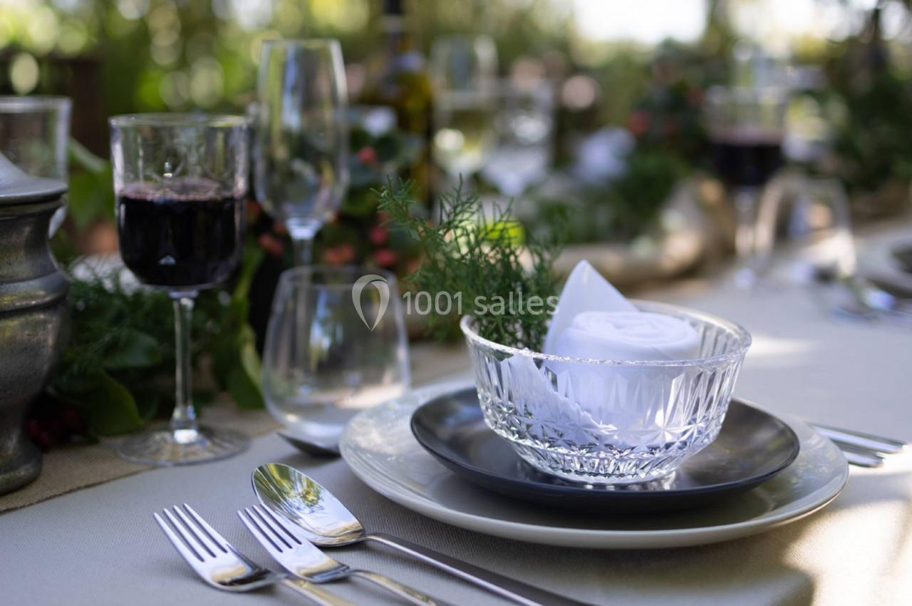 Table dressée avec des couverts, un verre de vin rouge, des assiettes et une décoration végétale en arrière-plan.