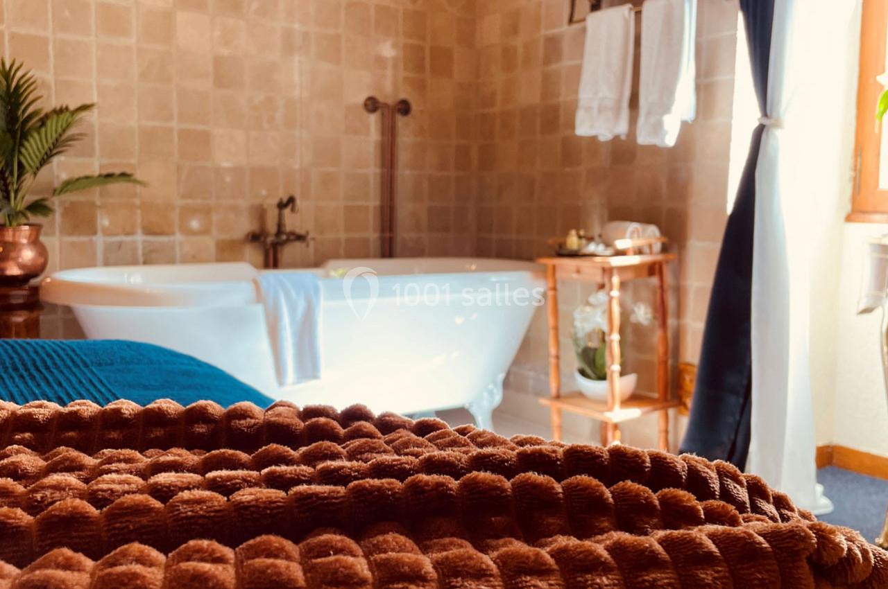 Salle de bain avec baignoire sur pieds, serviettes pliées au premier plan et lumière naturelle entrant par une fenêtre.