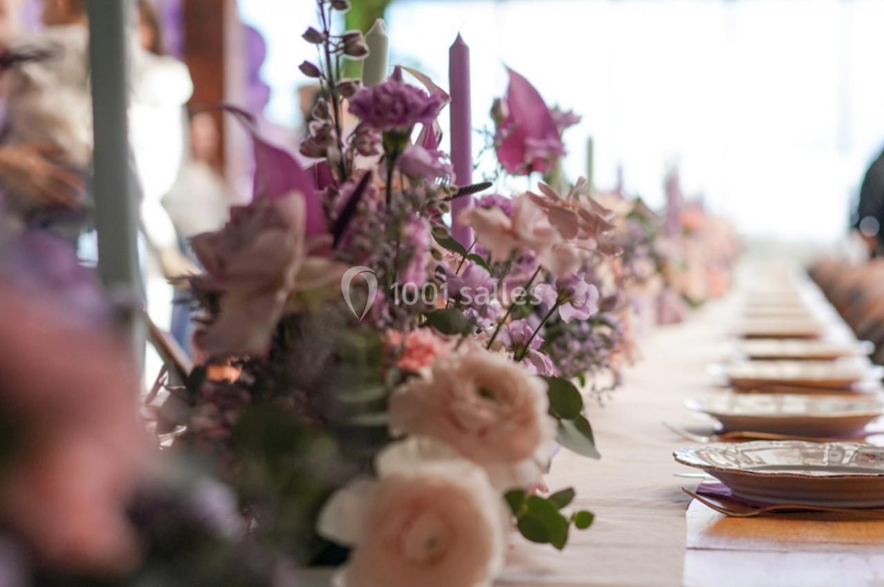 Table décorée avec des fleurs pastel et des bougies, alignée avec des assiettes dans un cadre lumineux.