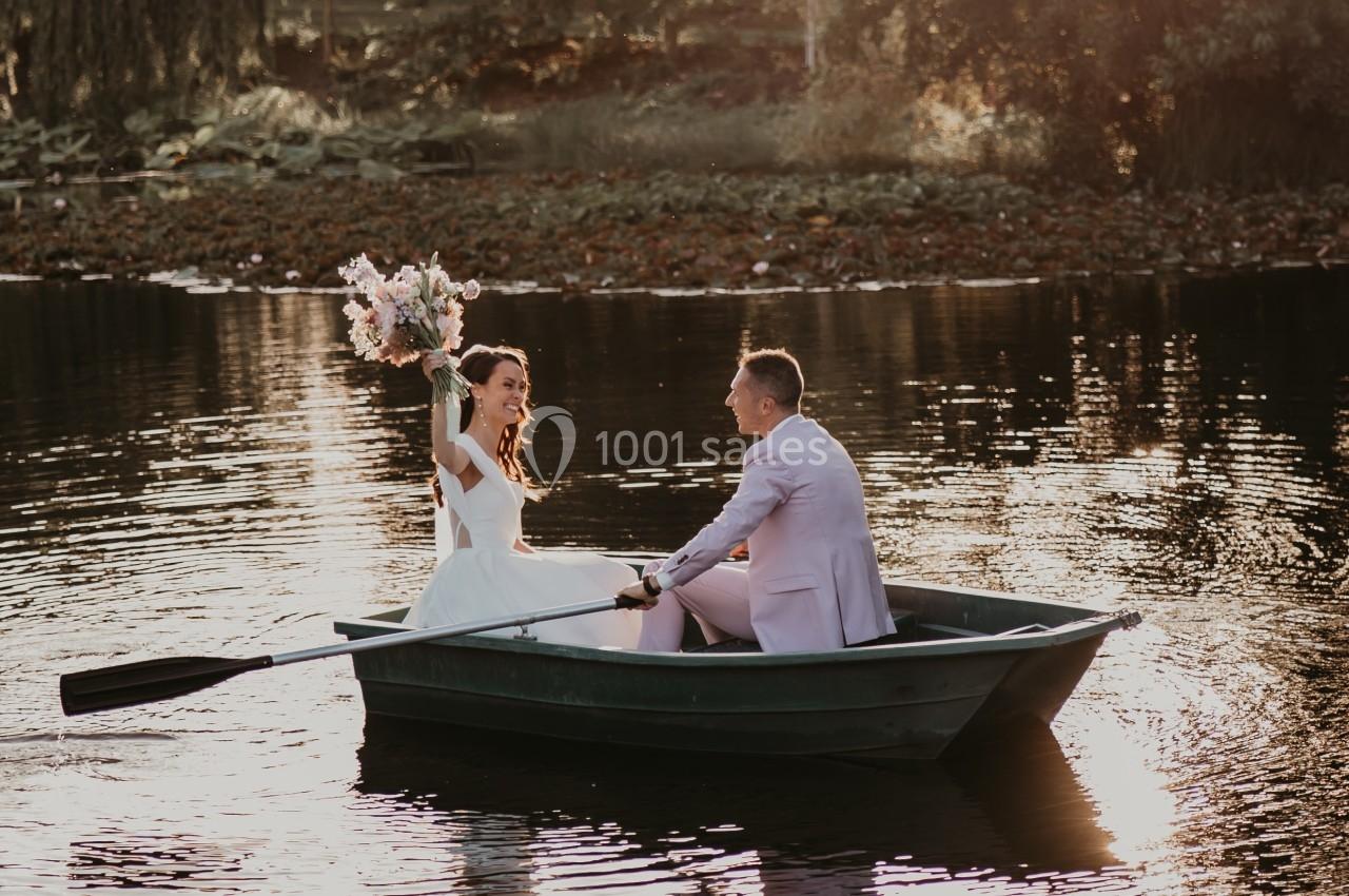 Un couple dans une barque sur un lac au coucher du soleil, la femme tenant un bouquet de fleurs.