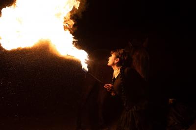 Une femme jongle avec des anneaux enflammés lors d'une performance nocturne en extérieur.