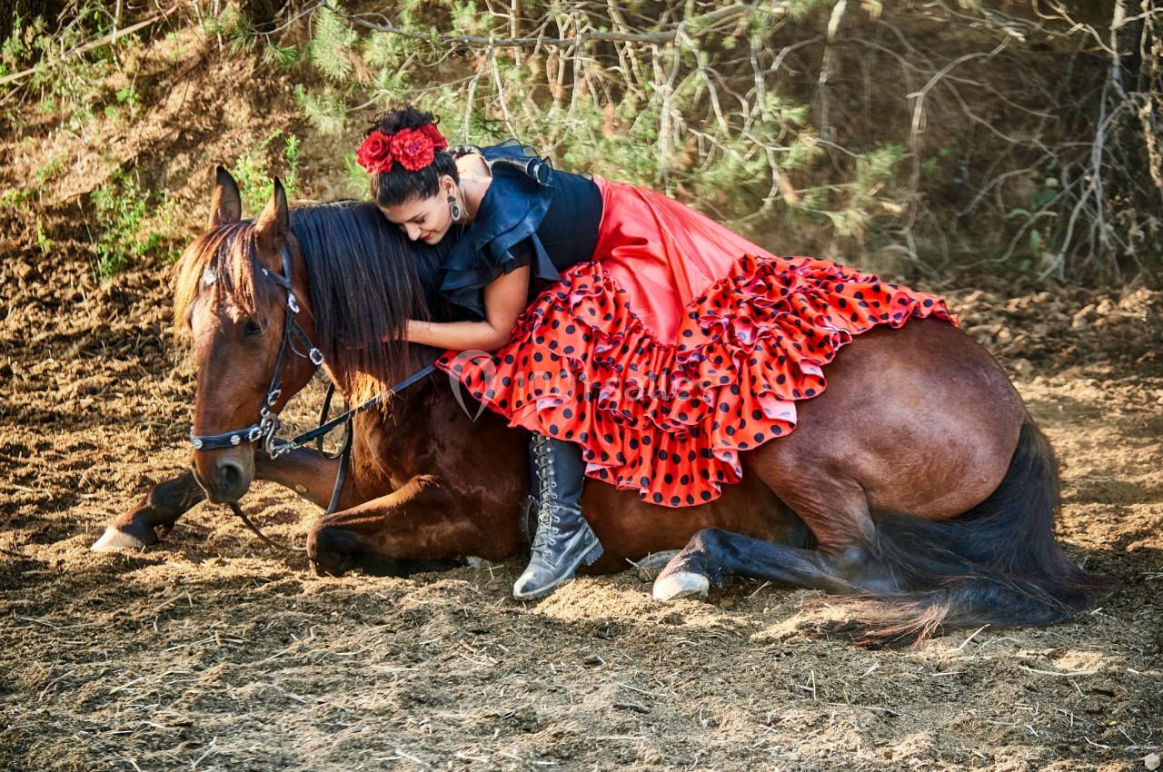 Femme en robe rouge à pois noirs allongée sur un cheval brun couché dans un environnement naturel.