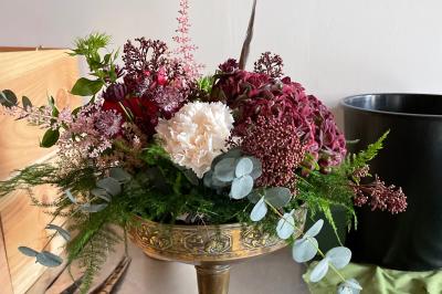 Composition florale dans une coupe en métal doré, avec des fleurs rouges, blanches et feuillages verts.