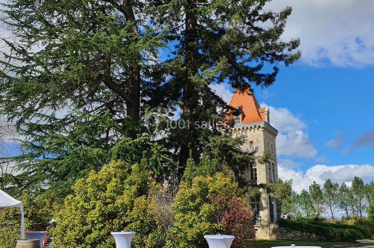 Tables hautes recouvertes de nappes blanches disposées en extérieur devant un château entouré de verdure.