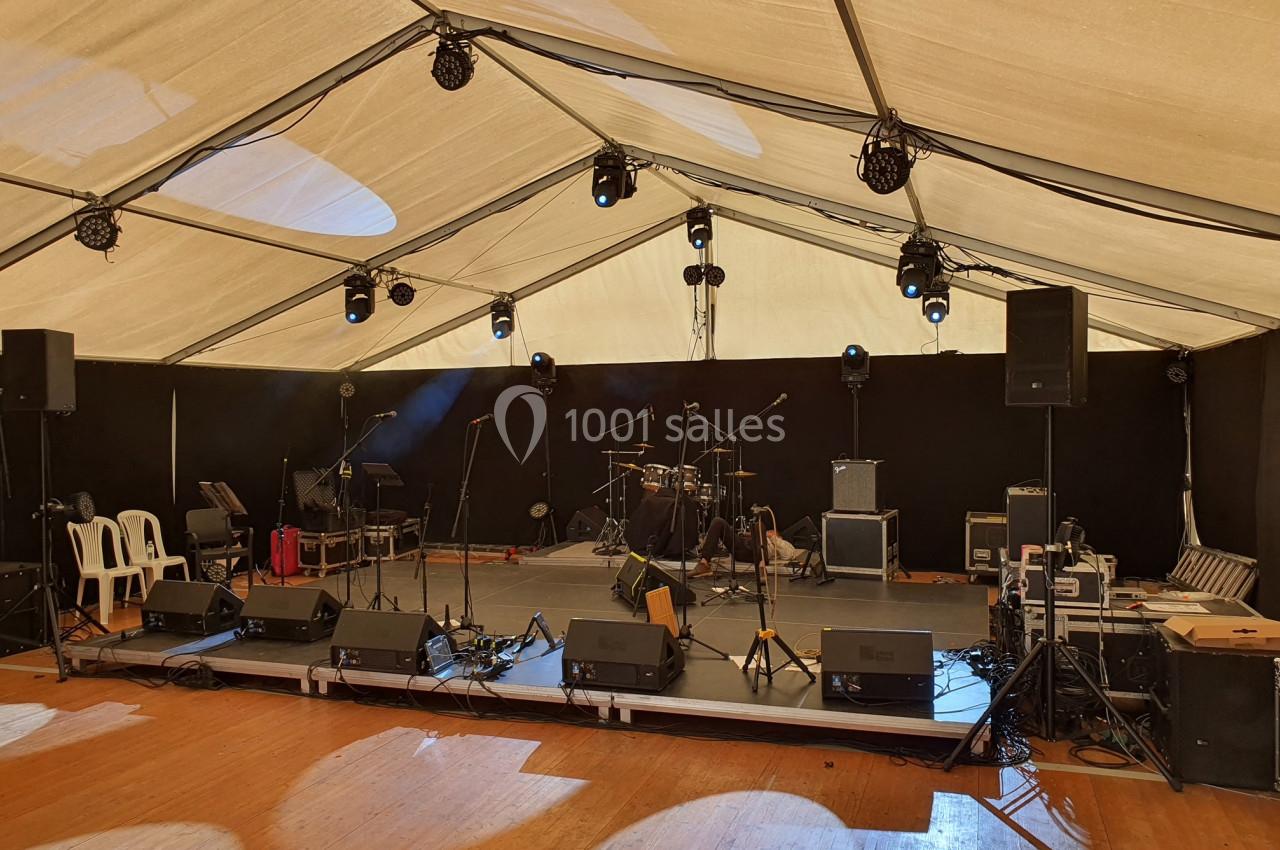 Scène vide sous un chapiteau, équipée de micros, enceintes, amplificateurs et batterie, prête pour un concert.