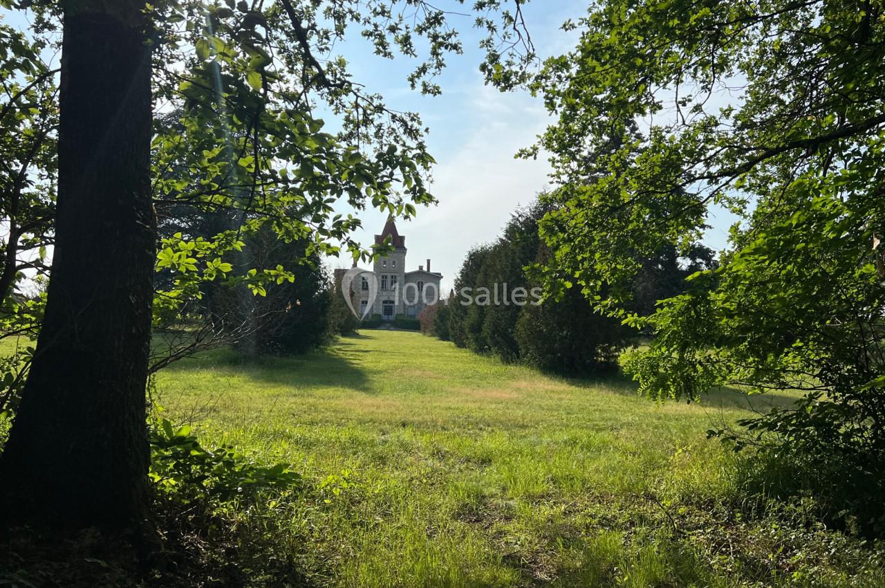 Vue d'un château au loin, entouré d'arbres et donnant sur une vaste pelouse sous un ciel dégagé.
