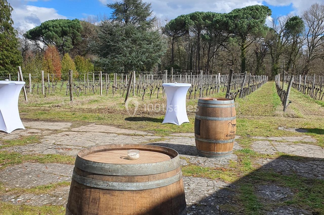 Vue d'un vignoble avec des tonneaux en bois au premier plan et des tables hautes blanches en arrière-plan.