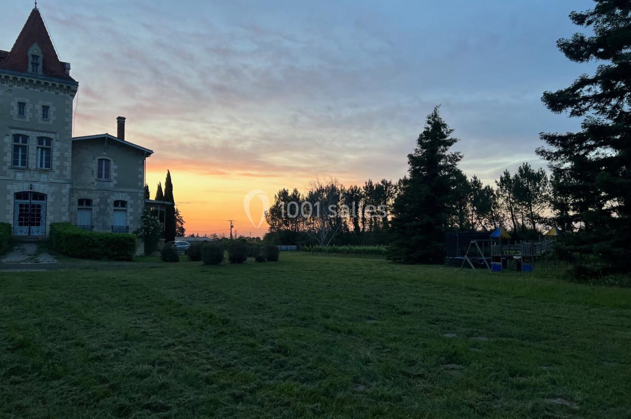 Château en pierre avec tour, entouré de pelouse et d'arbres, au coucher du soleil.