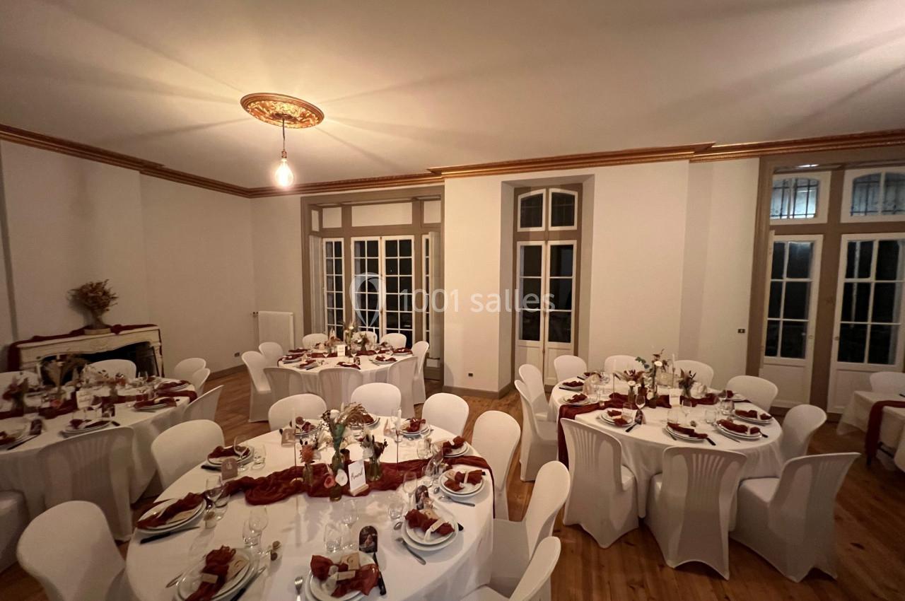 Salle de réception élégante avec tables rondes dressées, nappes blanches et décorations florales.
