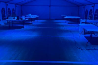 Intérieur d'une tente éclairée en rouge, avec des tables rondes et des chaises blanches disposées pour un événement.