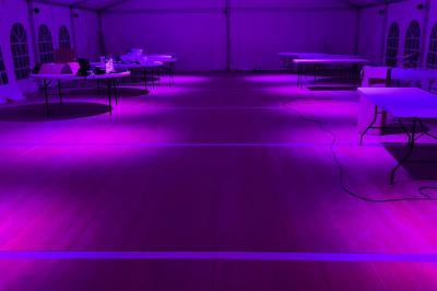 Intérieur d'une tente éclairée en rouge, avec des tables rondes et des chaises blanches disposées pour un événement.