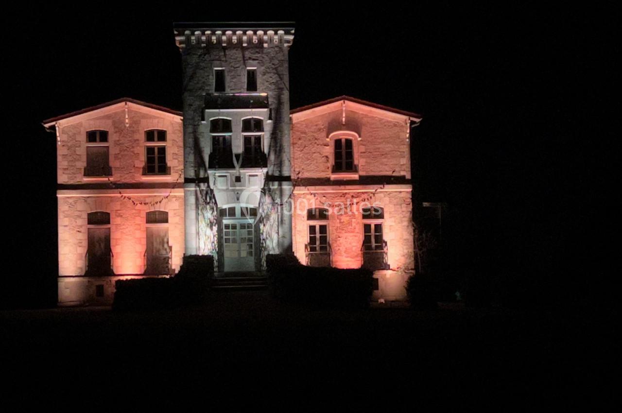 Façade d'un bâtiment en pierre éclairée par des lumières rouges et blanches, de nuit.