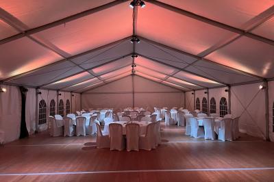Intérieur d'une tente éclairée en rouge, avec des tables rondes et des chaises blanches disposées pour un événement.