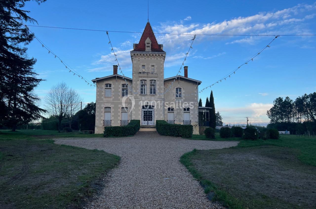 Façade d'un château en pierre avec une tour centrale, entouré de végétation et éclairé par des guirlandes suspendues.