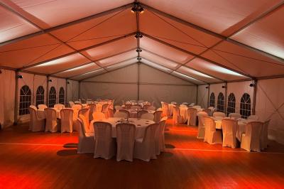 Intérieur d'une tente éclairée en rouge, avec des tables rondes et des chaises blanches disposées pour un événement.
