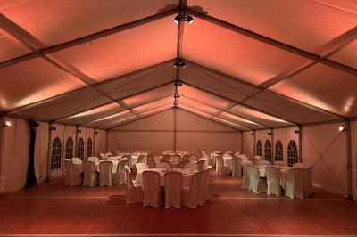 Intérieur d'une tente éclairée en rouge, avec des tables rondes et des chaises blanches disposées pour un événement.
