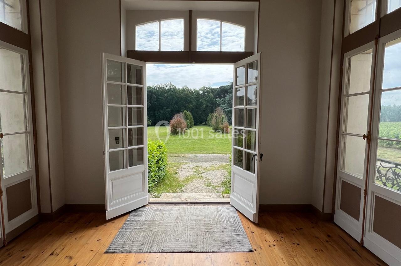 Vue depuis une pièce lumineuse avec parquet, montrant des portes-fenêtres ouvertes sur un jardin verdoyant.