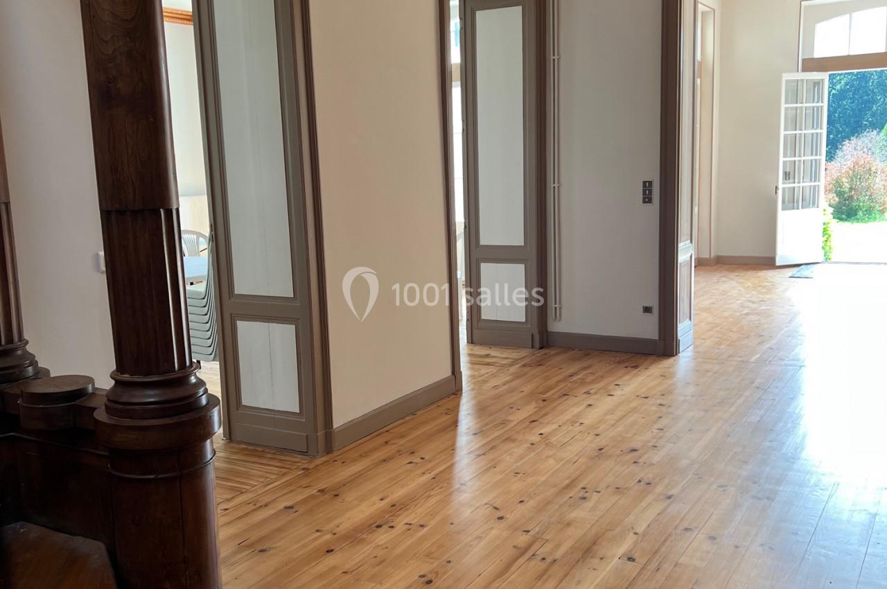 Intérieur lumineux avec parquet en bois, portes ouvertes sur un jardin et escalier en bois au premier plan.