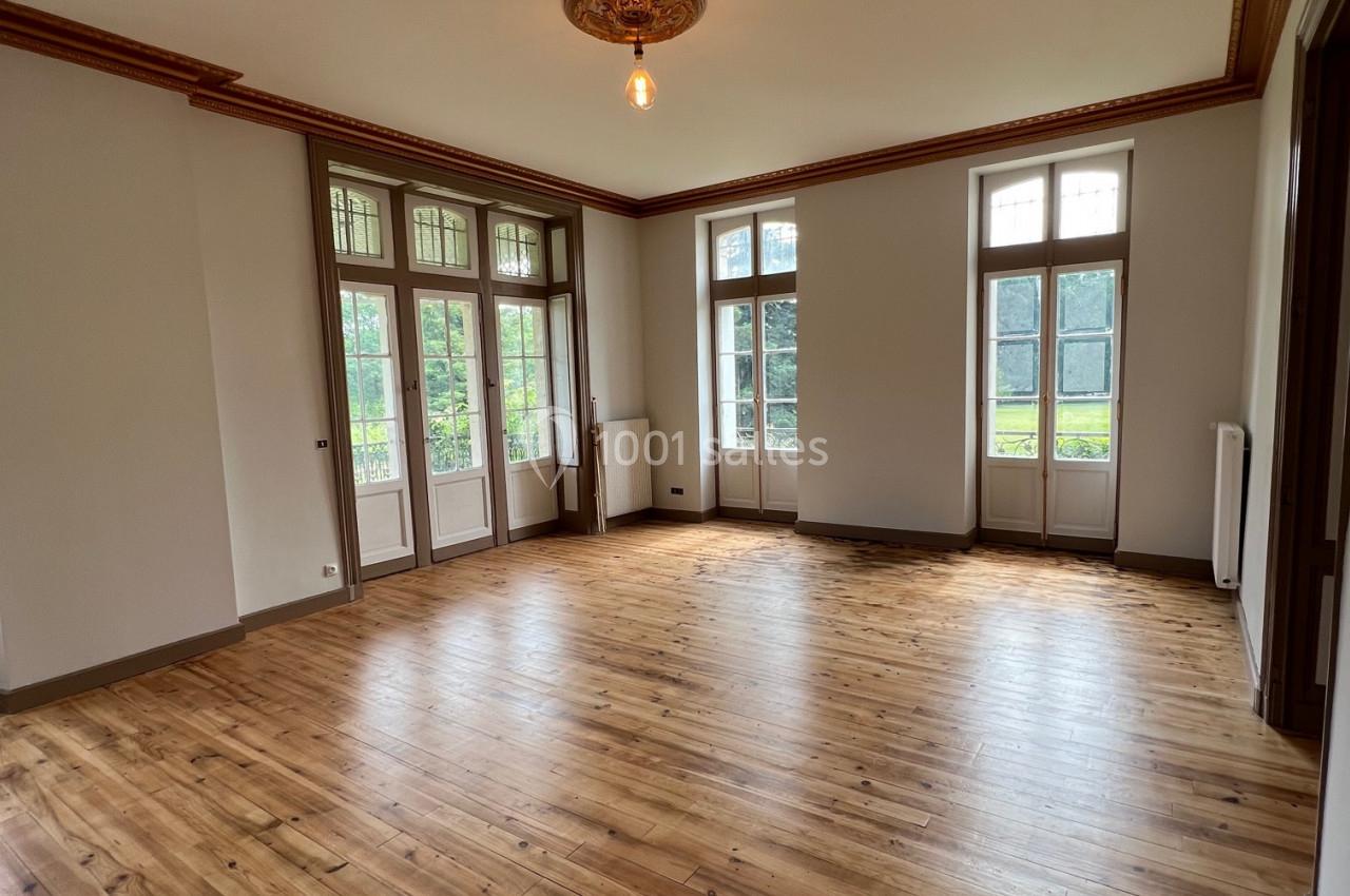 Salle lumineuse avec parquet en bois, grandes fenêtres donnant sur un jardin et moulures au plafond.