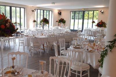 Salle de réception sous une tente avec tables dressées, décorations florales et éclairage suspendu.