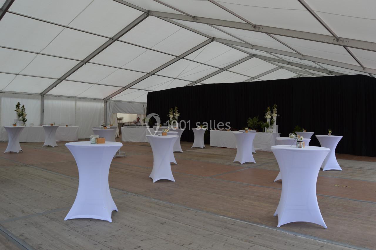 Intérieur d'une tente événementielle avec des tables hautes drapées de blanc et un fond de rideaux noirs.