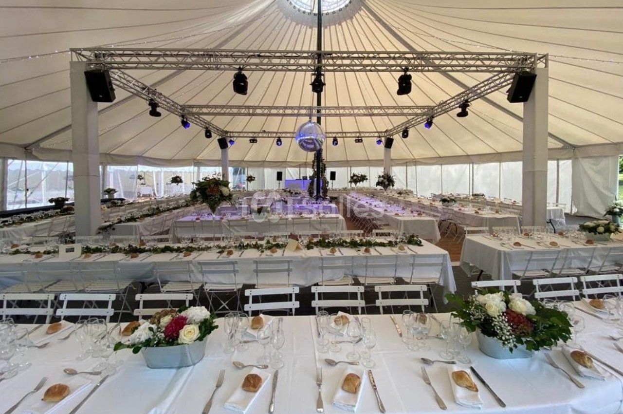 Intérieur d'une tente de réception avec tables dressées, décor floral et éclairage suspendu.