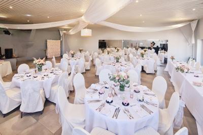 Salle de réception élégante décorée de nappes blanches, chaises habillées et centres de table floraux.