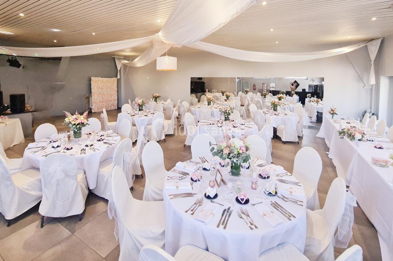 Salle de réception décorée avec des tables rondes dressées, nappes blanches et arrangements floraux.