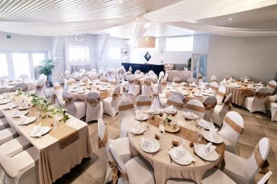 Salle de réception élégante décorée de nappes blanches, chaises habillées et centres de table floraux.
