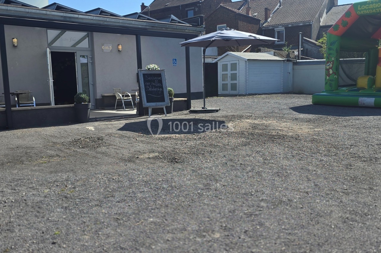 Cour extérieure avec une structure gonflable colorée, une terrasse aménagée et un tableau noir près de l'entrée.