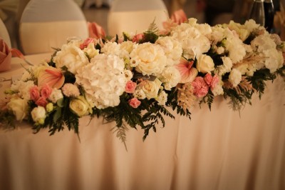 Salle de réception élégante décorée de nappes blanches, chaises habillées et centres de table floraux.