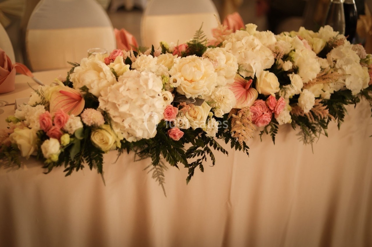 Arrangement floral avec des roses, des hortensias et des feuillages, disposé sur une table recouverte d'une nappe beige.