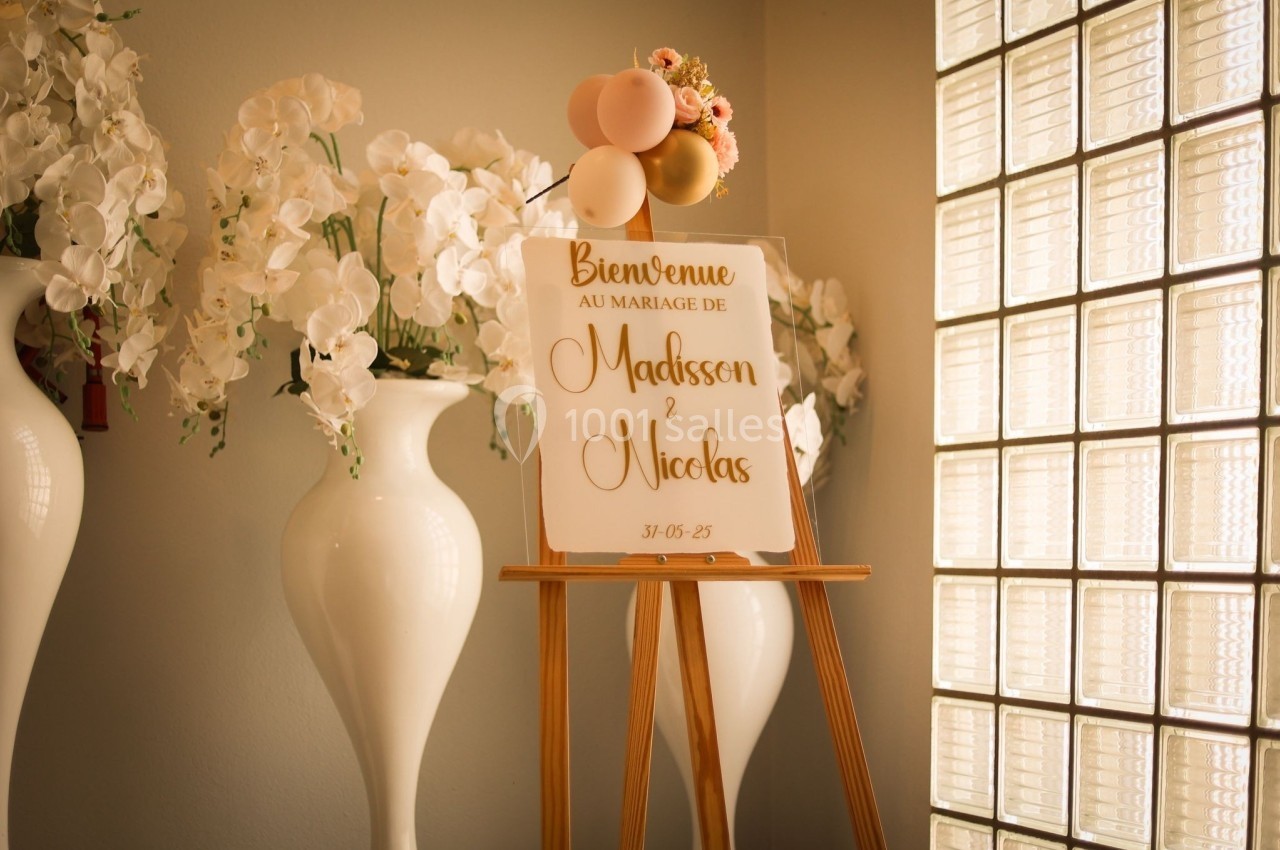 Panneau de bienvenue pour un mariage, posé sur un chevalet, entouré de vases blancs avec des fleurs.