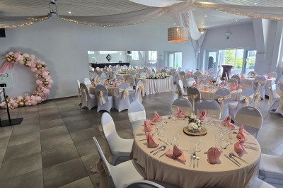 Salle de réception élégante décorée de nappes blanches, chaises habillées et centres de table floraux.