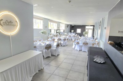 Salle de réception élégante décorée de nappes blanches, chaises habillées et centres de table floraux.