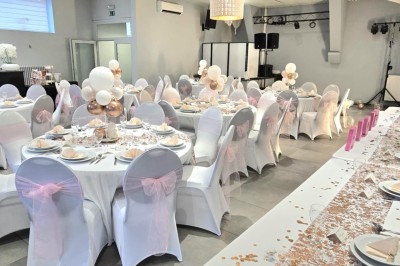 Salle de réception élégante décorée de nappes blanches, chaises habillées et centres de table floraux.