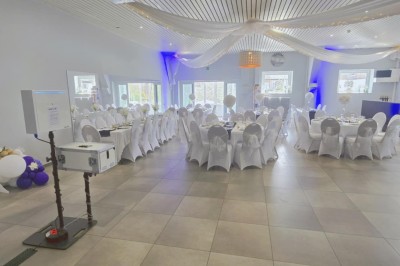 Salle de réception élégante décorée de nappes blanches, chaises habillées et centres de table floraux.