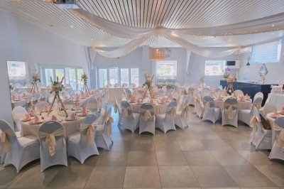 Salle de réception élégante décorée de nappes blanches, chaises habillées et centres de table floraux.