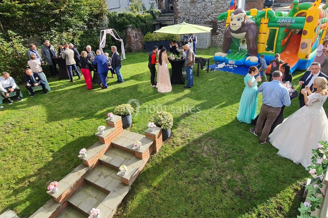 Groupe de personnes rassemblées dans un jardin pour une fête, avec une structure gonflable et des décorations florales.