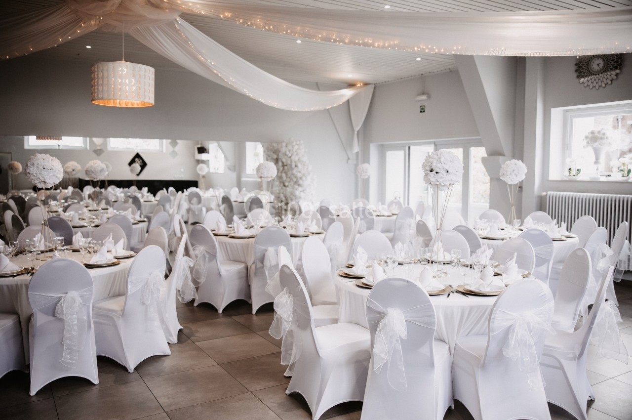 Salle de réception élégante décorée de nappes blanches, chaises habillées et centres de table floraux.