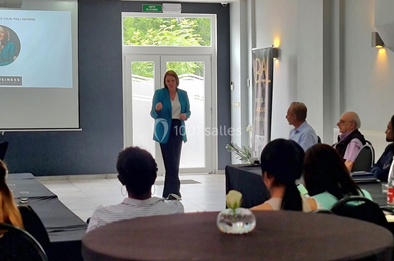 Une femme donne une présentation devant un public assis dans une salle de conférence lumineuse.