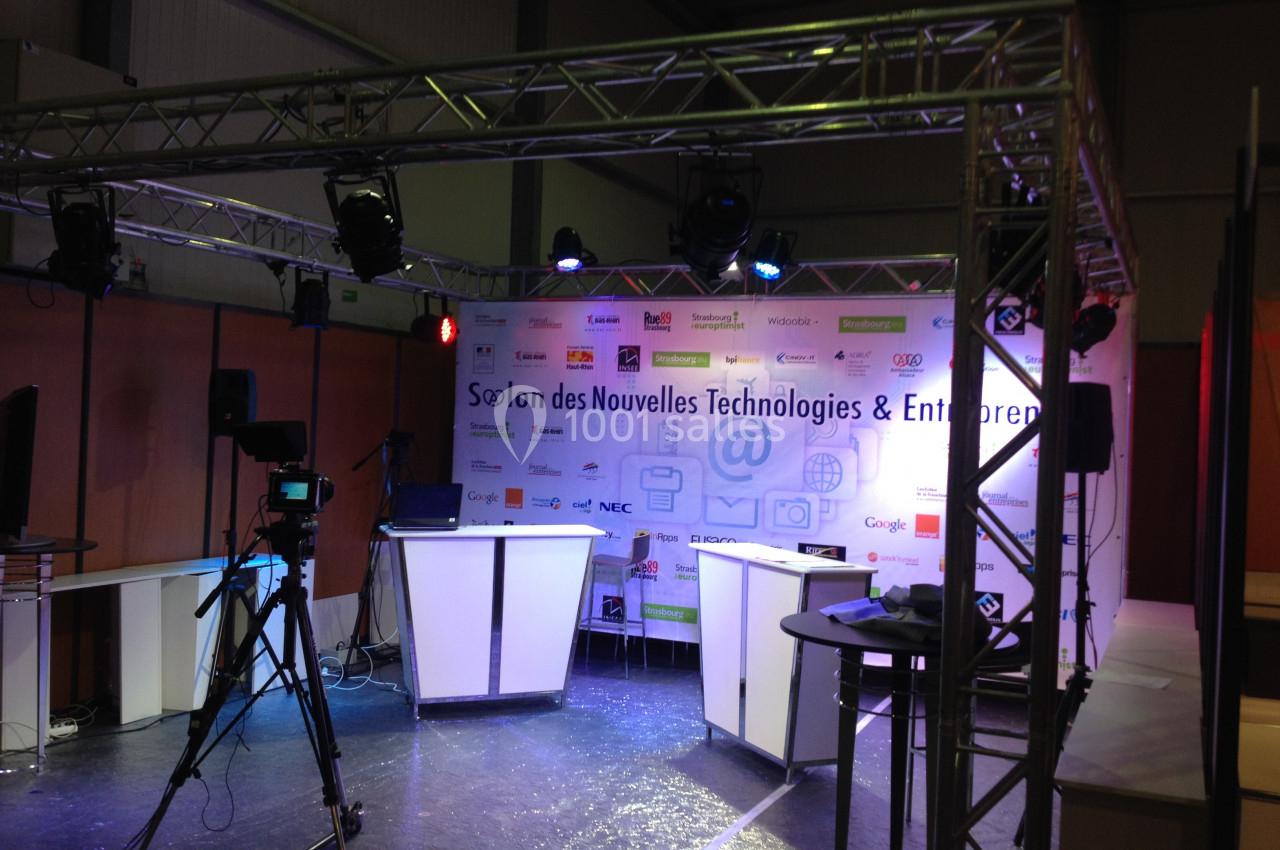 Scène d'exposition avec éclairage, caméras et fond affichant des logos d'entreprises technologiques.