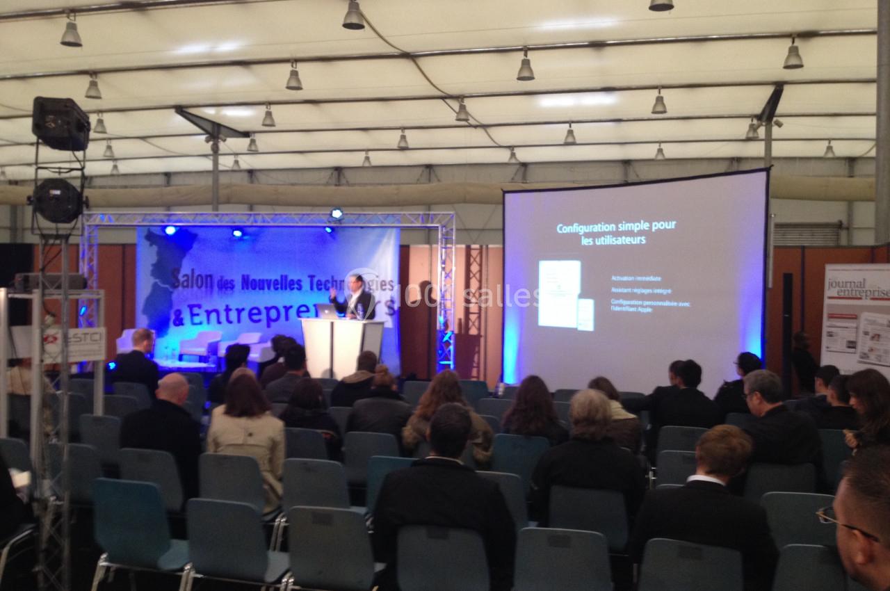 Conférence dans un salon professionnel avec des participants assis et une présentation projetée sur écran.