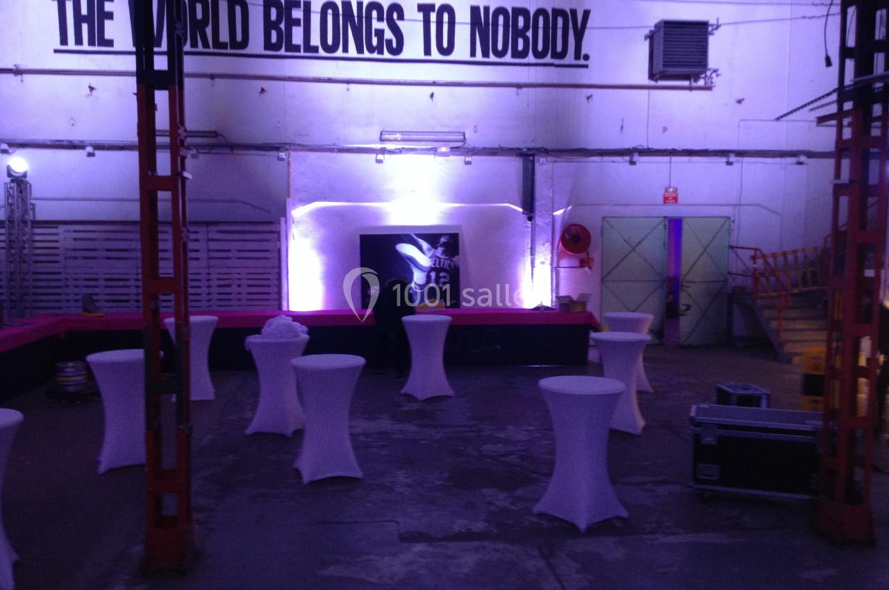 Salle industrielle aménagée avec des tables hautes blanches, éclairage violet et inscription murale ’The world belongs to…